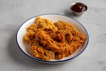 Chicken Popcorn, Wings and Tenders with BBQ Sauce on a plate on a gray background, side view.