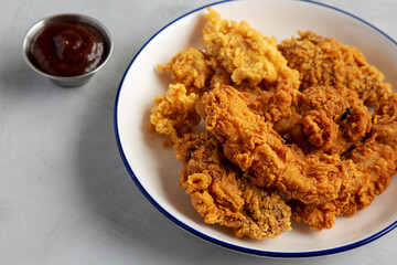 Chicken Popcorn, Wings and Tenders with BBQ Sauce on a plate on a gray background, side view.