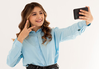 Image of beautiful brunette woman laughing and showing peace sign while taking selfie photo on...