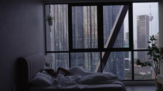 Morning in hotel room. Young woman sleep on comfortable bed . Window of a skyscraper on background.