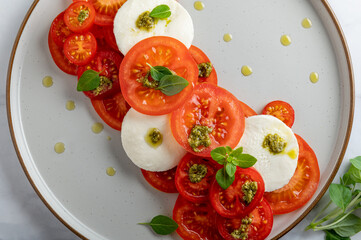 Classic italian salad caprese served in original form with different tomatoes, mozarella, pesto sauce and basil