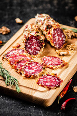 Pieces of salami sausage on a cutting board with pods of dried chili peppers. 
