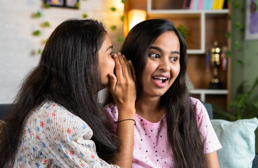 young teenager girl sharing secrets to sisterat home - concept of whispering, communication and trust.