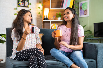 Happy smiling siblings talking eachother by drinking tea or coffee at home - concept of friendship,...