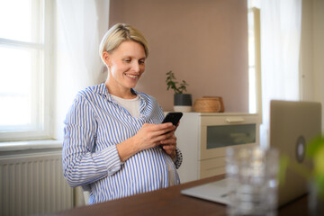 Pregnant woman having home office, scrolling her phone.