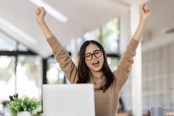 Portrait of Happy Excited young asian woman at workplace office desk, successful Asian female reading good news technology online, employee freelance finance concepts.