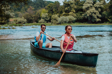 Couple adventurous explorer friends are canoeing in a wild river surrounded by the beautiful nature