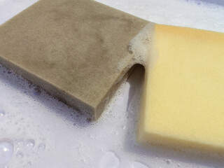 two pieces of yellow and gray rectangular cleaning sponges with white soap bubbles in a laundry room