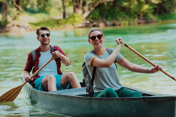 Couple adventurous explorer friends are canoeing in a wild river surrounded by the beautiful nature