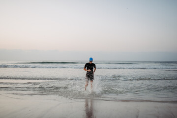 Woman in neoprene running out of the ocean.