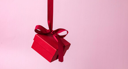 Red gift box with a ribbon hangs on a pink background. Gift on Valentine's Day, Women's Day,