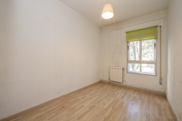 Small empty room with laminated flooring, aluminum window with green roller blind and white aluminum radiator