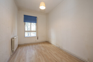 Old bedroom with a small aluminum window with a blue shutter, walls in need of a coat of paint and laminated flooring