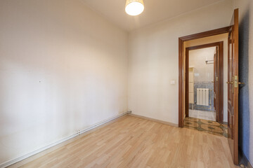 Small empty room with a laminate floor and a sapele wood access door next to a bathroom with a radiator