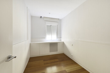 Empty room with wooden floors, plain white walls and white woodwork under the window