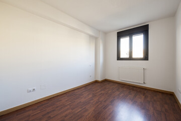 Empty room of a house with a dark colored laminate floor and a dark anodized aluminum window and a radiator below