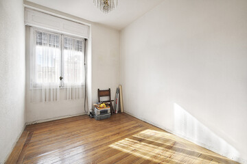 empty room of a house with a floor of beautiful pine driftwood flooring with a window with white curtains and some old objects in the corner
