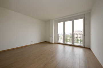Empty room with light wooden floors and a balcony with three aluminum and glass doors with views