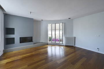 Fototapeta na wymiar Empty living room with a dark oak hardwood floor, smooth light blue-grey walls, a built-in fireplace in the wall, and access to a terrace with awnings