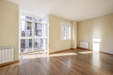 Empty room with light oak hardwood floors in a house with a white aluminum and glass bay window and matching windows