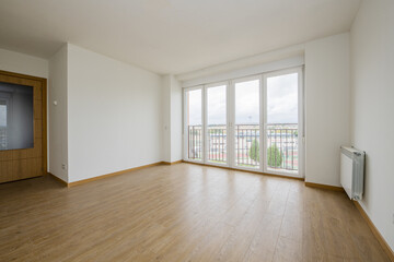 Empty room with light wooden floors, white aluminum radiators, smooth white painted walls, oak and glass front door and blacond e four aluminum and glass doors with views of the city