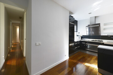 Kitchen with glossy black wood cabinets with white countertops, stainless steel appliances, dark hardwood floors, and long hallway with recessed lighting