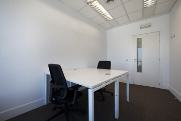 Office with double white wooden tables with white methacrylate dividers and black swivel stools and a door with elongated glass