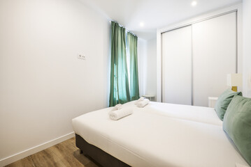 Fototapeta na wymiar Bedroom with a two-section built-in wardrobe with white sliding doors, single beds together with trundles and green curtains