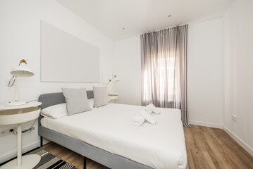 Bedroom with white and gray furniture, double bed with fabric headboard and white ederedon, curtains on the window and wooden flooring