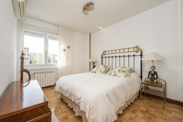 Bedroom with wooden furniture, double bed with metal headboard and fringed bedspread and window with views
