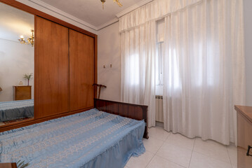A room with a double bed without a mattress, a built-in wardrobe and a window with curtains