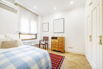 Room with a double bed with a blue plaid blanket, a vintage-style wooden chest of drawers and a...