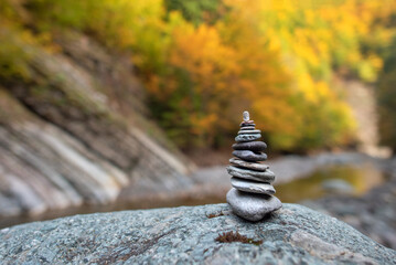 Fototapeta na wymiar Stone stack with balanced stones on blurred mountain background in sunset warm light in autumn foliage