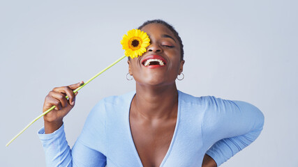  Portrait of a happy young woman holding orange Gerbera daisy covering her eye with eyes closed