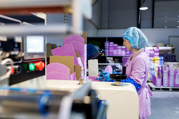 Professional female worker in uniform and protective gloves packed chocolate candies in boxes on...