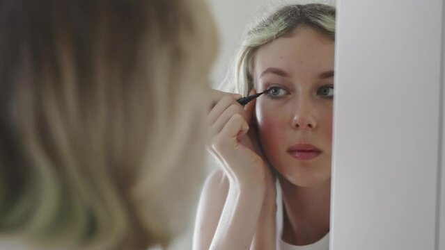 Teenage girl doing makeup with black eyeliner.