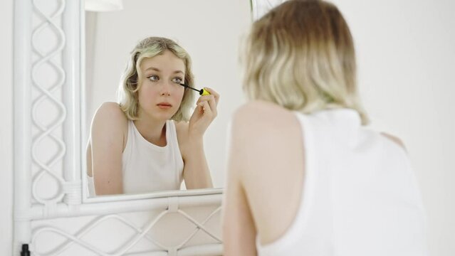Teenage girl applying black mascara on lashes.