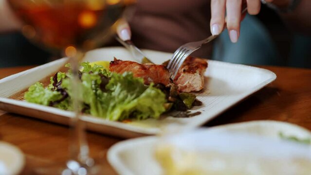 A girl cuts a steak on a plate with a fork and a knife, close-up. Dinner in a restaurant