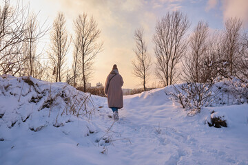 A young woman walks in the snow on a sunny frosty day, enjoying winter moments and nature, wearing winter clothes. Winter time concept, walk