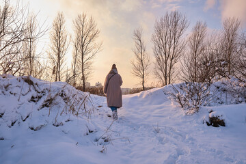 Fototapeta premium A young woman walks in the snow on a sunny frosty day, enjoying winter moments and nature, wearing winter clothes. Winter time concept, walk