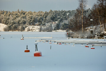 Winter seascape with white snow at an empty boat harbour with jetty and red buoys in the frozen Lake Mälaren in Sweden.