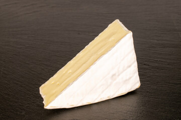 One piece of fragrant brie cheese on slate stone, macro.