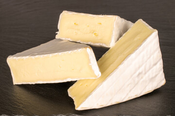 Three pieces of fragrant Brie cheese on slate stone, macro.
