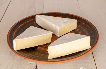 Three slices of delicious brie cheese with a clay plate on a wooden table, macro.