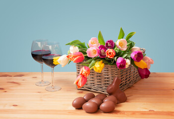 Easter concept. Colorful tulips, chocolate bunny, glasses of red wine and chocolate Easter eggs on wooden table.