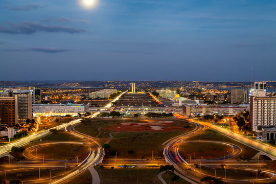 Brasilia city in a colorful long exposure shot during night. Aerial view of the city structure. The congress and ministries are visible far away. Full moon above the sky.
