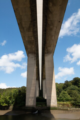 View from under an highway bridge crossing a river. A blue sky with white clouds behind.