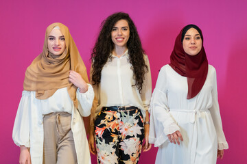 Fototapeta na wymiar Group portrait of beautiful muslim women two of them in fashionable dress with hijab isolated on pink background representing modern islam fashion and ramadan kareem concept