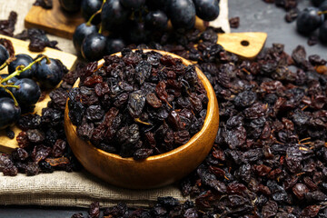 Dried black raisins in wooden bowl, woden background. Selective focus