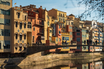 Fototapeta na wymiar View of bright traditional Mediterranean houses on the canal's banks on a sunny day. People walk on the bridge in Girona city.